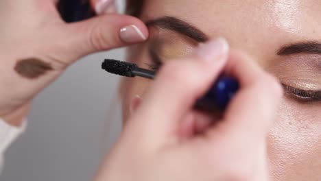 Master-is-using-black-mascara-on-womans-eyes,-performing-make-up