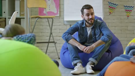 Hombre-joven-hablando-con-los-niños-en-aula-de-jardín-de-infantes