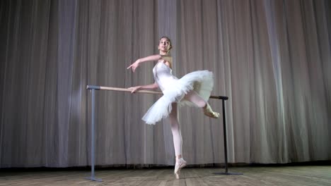 Ballett-Probe-im-alten-Theatersaal.-Jungen-Ballerina-in-weißen-Ballett-Rock-Tutu,-engagiert-beim-Ballett,-führt-elegant-eine-gewisse-Ballett-Bewegung,-Haltung-Allonge,-stehen-in-der-Nähe-von-Barre