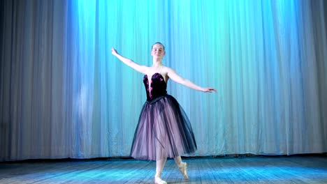 ballet-rehearsal,-on-the-stage-of-the-old-theater-hall.-Young-ballerina-in-lilac-black-elegant-dress-and-pointe-shoes,-dances-elegantly-certain-ballet-motion,-assemble-ferme