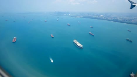 Travel-video-View-from-the-airplane-window-through-the-wings-and-engine-Flying-through-the-ocean-and-the-cargo-ship-is-sailing-in-the-sea-near-the-shipping-port-in-transportation-or-travel-concept.