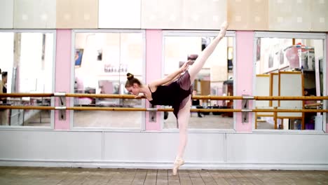 en-baile-de-salón,-joven-bailarina-en-leotardo-púrpura-elegante-realiza-un-determinado-ejercicio-de-ballet,-arabesque-en-pendiente,-de-pie-junto-a-la-barra-en-espejo-en-clase-de-ballet