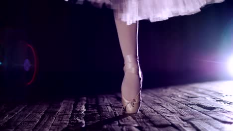 close-up,-in-rays-of-spotlight,-on-stage-of-old-theater-hall.-ballerina-in-white-ballet-skirt,-rotates-on-toe-in-pointe-shoe,-performs-elegantly-a-certain-ballet-exercise,-tour,pointe