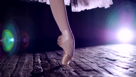 close-up,-in-rays-of-spotlight,-on-stage-of-old-theater-hall.-ballerina-in-white-ballet-skirt,-rotates-on-toe-in-pointe-shoe,-performs-elegantly-a-certain-ballet-exercise,-tour,pointe