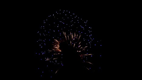 Fuegos-artificiales-en-el-cielo-de-una-noche-oscura.-Impresionante-hermosas-luces-en-el-centro-se-llena-de-gente,-largos-hilos-de-chispas-divergen-desde-ambos-lados,-luces-azules-se-encuentran-dispersos-por-todo-el-cielo