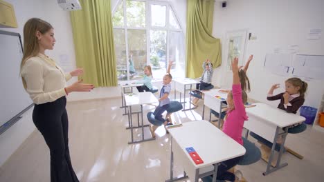 professional-teacher-woman-talks-to-little-cute-children-pupils-at-desks-during-education-lesson-in-classroom-at-school