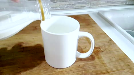 fresh-white-milk-pouring-into-drinking-glass-on-kitchen-background,-shooting-with-slow-motion,-diet-and-healthy-nutrition-breakfast