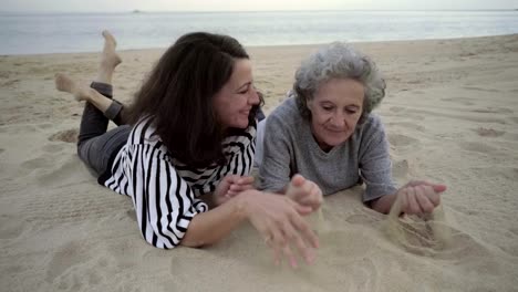 Ältere-Mutter-und-Tochter-spielen-mit-Sand-und-am-Strand-liegen