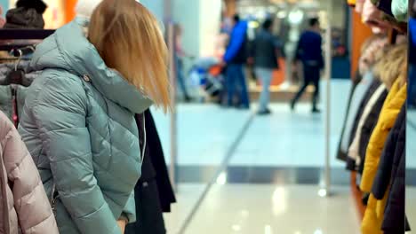 Eine-Frau-wählt-eine-Daunenjacke.-In-der-Oberbekleidung-store