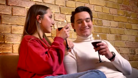 Retrato-de-joven-pareja-caucásica-sentado-en-el-sofá-y-bebiendo-vino-hablando-con-los-demás-en-el-acogedor-ambiente-de-casa.