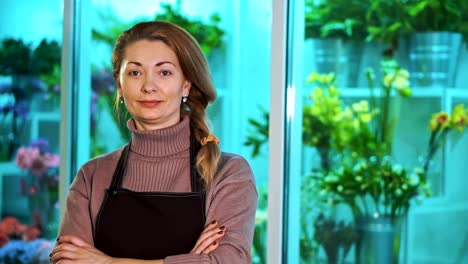 Frau-Florist-schaut-die-Kamera-auf-dem-Hintergrund-der-Schaufenster-von-Blumen.