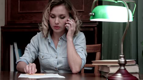 Tired-young-woman-sitting-at-her-desk-receiveing-very-bad-news-on-the-phone