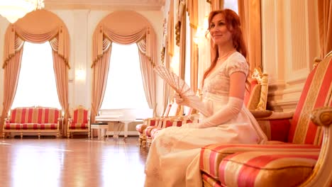 Mujer-atractiva-en-un-traje-de-la-bola-blanca-con-el-ventilador-en-la-mano-posando-en-la-sala-de-la-bola