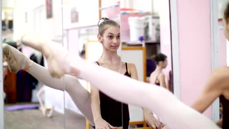 in-dancing-hall,-Young-ballerina-in-purple-leotard-performs-developpe-aside-on-pointe-shoes,-raises-her-leg-up-elegantly,-standing-near-barre-at-mirror-in-ballet-class.-close-up