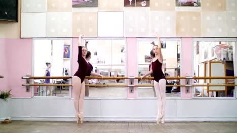 in-dancing-hall,-Young-ballerinas-in-purple-leotards-perform-grand-battement-back-on-pointe-shoes,-raise-their-legs-up-elegantly,-standing-near-barre-at-mirror-in-ballet-class