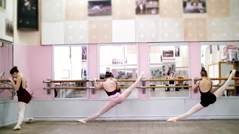 en-salón-de-baile,-jóvenes-bailarinas-en-negro-leotardos-estiramiento-en-barra,-en-los-zapatos-del-pointe,-elegantemente,-de-pie-cerca-barre-en-espejo-en-clase-de-ballet