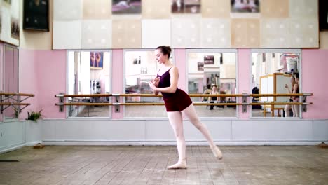 in-dancing-hall,-Young-ballerina-in-black-leotard-performs-grand-battement-back,-raises-her-leg-up-behind-elegantly,-in-ballet-class