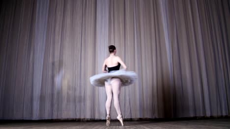 ballet-rehearsal,-on-the-stage-of-the-old-theater-hall.-Young-ballerina-in-white-ballet-tutu-and-pointe-shoes,-dances-elegantly-certain-ballet-motion,-tour-chaines