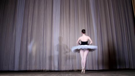 ballet-rehearsal,-on-the-stage-of-the-old-theater-hall.-Young-ballerina-in-white-ballet-tutu-and-pointe-shoes,-dances-elegantly-certain-ballet-motion,-glissad-en-tornant