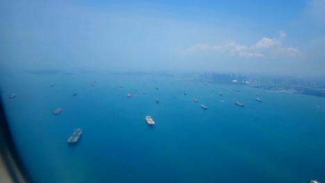 Travel-video-View-from-the-airplane-window-through-the-wings-and-engine-Flying-through-the-ocean-and-the-cargo-ship-is-sailing-in-the-sea-near-the-shipping-port-in-transportation-or-travel-concept.