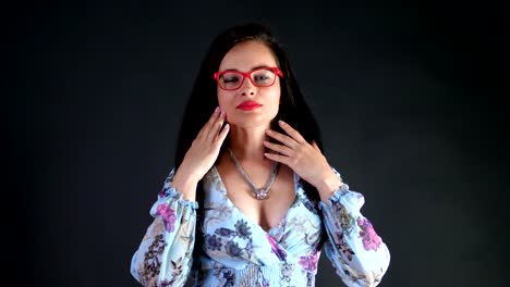 Retrato-de-una-atractiva-mujer-morena-con-rojo-labios-que-danza-y-juguetonamente-intenta-en-gafas-con-estilo,-gafas-y-sexualmente-mirando-a-cámara,-posando-en-el-estudio.-fondo-gris-oscuro