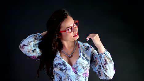 Retrato-de-una-atractiva-mujer-morena-con-rojo-labios-que-danza-y-juguetonamente-intenta-en-gafas-con-estilo,-gafas-y-sexualmente-mirando-a-cámara,-posando-en-el-estudio.-fondo-gris-oscuro