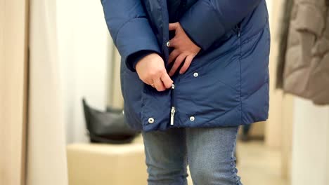 Woman-in-a-clothing-store,-close-up,-fastens-blue-down-jacket