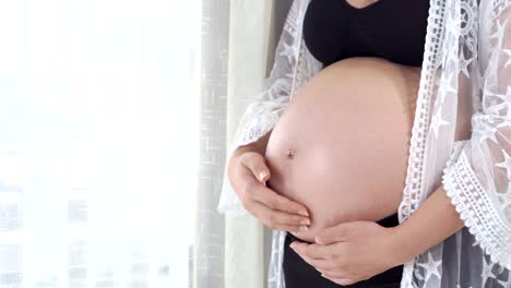 panning-shot-of-female-hands-pat-the-pregnant-belly