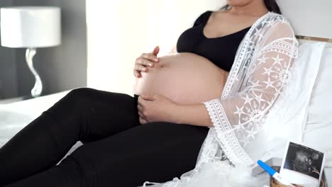 female-hands-pat-the-pregnant-belly-on-the-bed