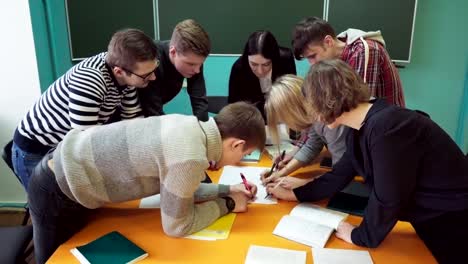 Jóvenes-estudiantes-con-un-maestro-escribiendo-y-discutiendo-algo-en-el-aula