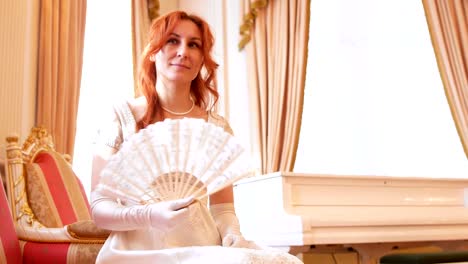 Beautiful-red-haired-woman-in-a-historical-ball-costume-posing-with-fan-in-her-hand