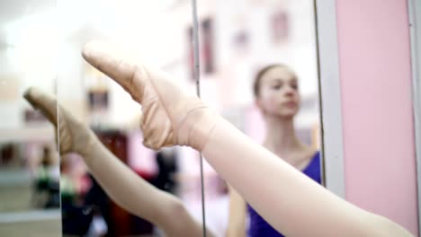 in-dancing-hall,-Young-ballerina-in-purple-leotard-performs-developpe-aside-on-pointe-shoes,-raises-her-leg-up-elegantly,-standing-near-barre-at-mirror-in-ballet-class.-close-up