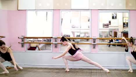 in-dancing-hall,-Young-ballerinas-in-black-leotards-are-stretching-parterre,-standing-near-barre-at-mirror-in-ballet-class