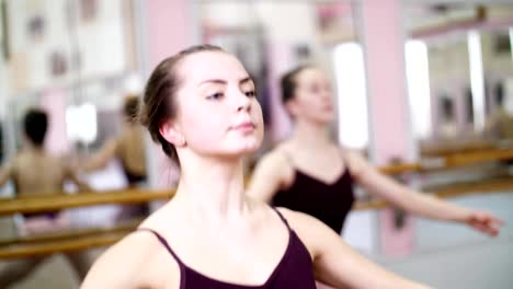 in-dancing-hall,-Young-ballerina-in-purple-leotard-performs-a-certain-ballet-exercise,-first-position-of-hands