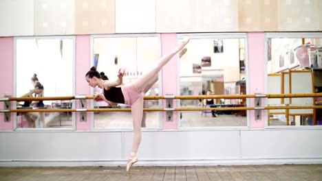 in-dancing-hall,-Young-ballerina-in-purple-leotard-performs-elegantly-a-certain-ballet-exercise,-arabesque-in-slope-,-standing-near-barre-at-mirror-in-ballet-class