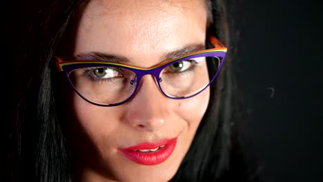 portrait-of-a-sexy-brunette-woman-with-red-lips-who-eroticly-and-playfully-tries-on-stylish-glasses,-spectacles-and-looking-sexually-at-camera-in-studio.-dark-gray-background