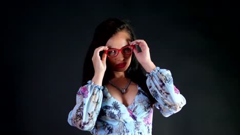 portrait-of-a-sexy-brunette-woman-with-red-lips-who-eroticly-and-playfully-tries-on-stylish-glasses,-spectacles-and-looking-sexually-at-camera,-posing-in-studio.-dark-gray-background