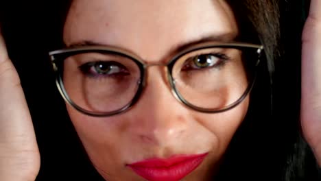 portrait-of-a-sexy-brunette-woman-with-red-lips-who-eroticly-and-playfully-tries-on-stylish-glasses,-spectacles-and-looking-sexually-at-camera-in-studio.-dark-gray-background