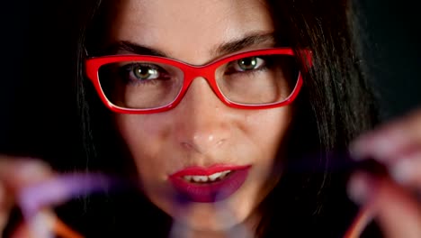 Retrato-de-una-atractiva-mujer-morena-con-rojo-los-labios-que-danza-y-juguetonamente-intenta-en-diferentes-pares-de-gafas-con-estilo,-espectáculos-y-sexualmente-mirando-a-cámara-en-estudio