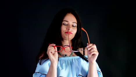 Retrato-de-una-atractiva-mujer-morena-con-rojo-los-labios-que-danza-y-juguetonamente-intenta-en-diferentes-pares-de-gafas-con-estilo,-espectáculos-y-sexualmente-mirando-a-cámara-en-estudio