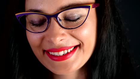 portrait-of-a-sexy-brunette-woman-with-red-lips-who-eroticly-and-playfully-tries-on-stylish-glasses,-spectacles-and-looking-sexually-at-camera-in-studio.-dark-gray-background