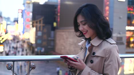 Pretty-happy-young-asian-woman-using-mobile-phone--in-the-Chinese-city-of-Chengdu-while-walking-on-the-overpass-with-busy-street-in-the-background