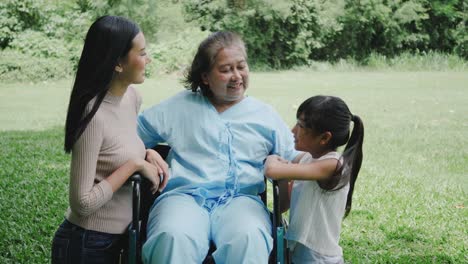 Grandmother-sitting-on-wheelchair-with-daughter-and-granddaughter-enjoy-in-the-park-together