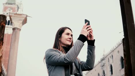 Atractivo-caucásico-mujer-turista-feliz-tomando-fotos-de-smartphone-de-antiguos-edificios-en-antigua-ciudad-de-Venecia.