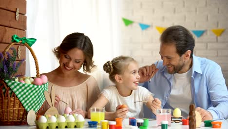 Father-tickling-ear-of-cute-daughter-with-paintbrush,-comfortable-family-evening