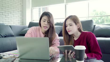 Lesbian-Asian-couple-using-laptop-making-budget-in-living-room-at-home,-sweet-couple-enjoy-love-moment-while-lying-on-the-sofa-when-relax-at-home.-Lifestyle-couple-relax-at-home-concept.