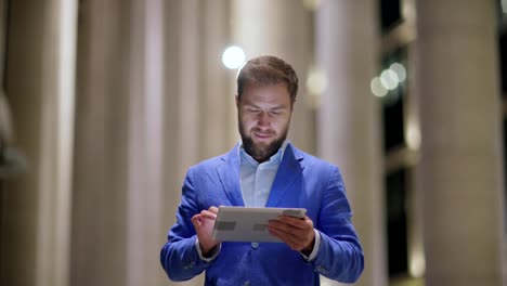 Bloqueo-de-la-cintura-para-la-foto-de-hombre-adulto-medio-sonriendo-mientras-intercambias-mensajes-en-tablet-PC-de-pie-al-aire-libre-en-la-noche