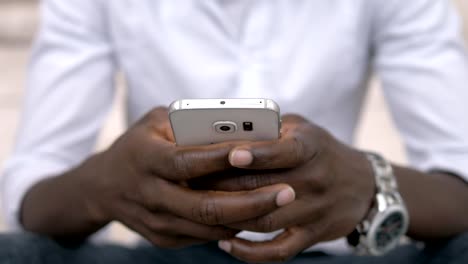 african-american-man's-hands-typing-on-smartphone--outdoor