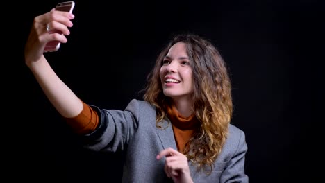 Closeup-portrait-of-positive-caucasian-young-female-taking-selfies-on-the-phone-smiling-and-posing