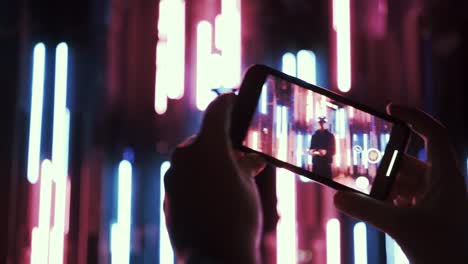 Detail-hands-with-phone-take-a-photo-in-neon-light